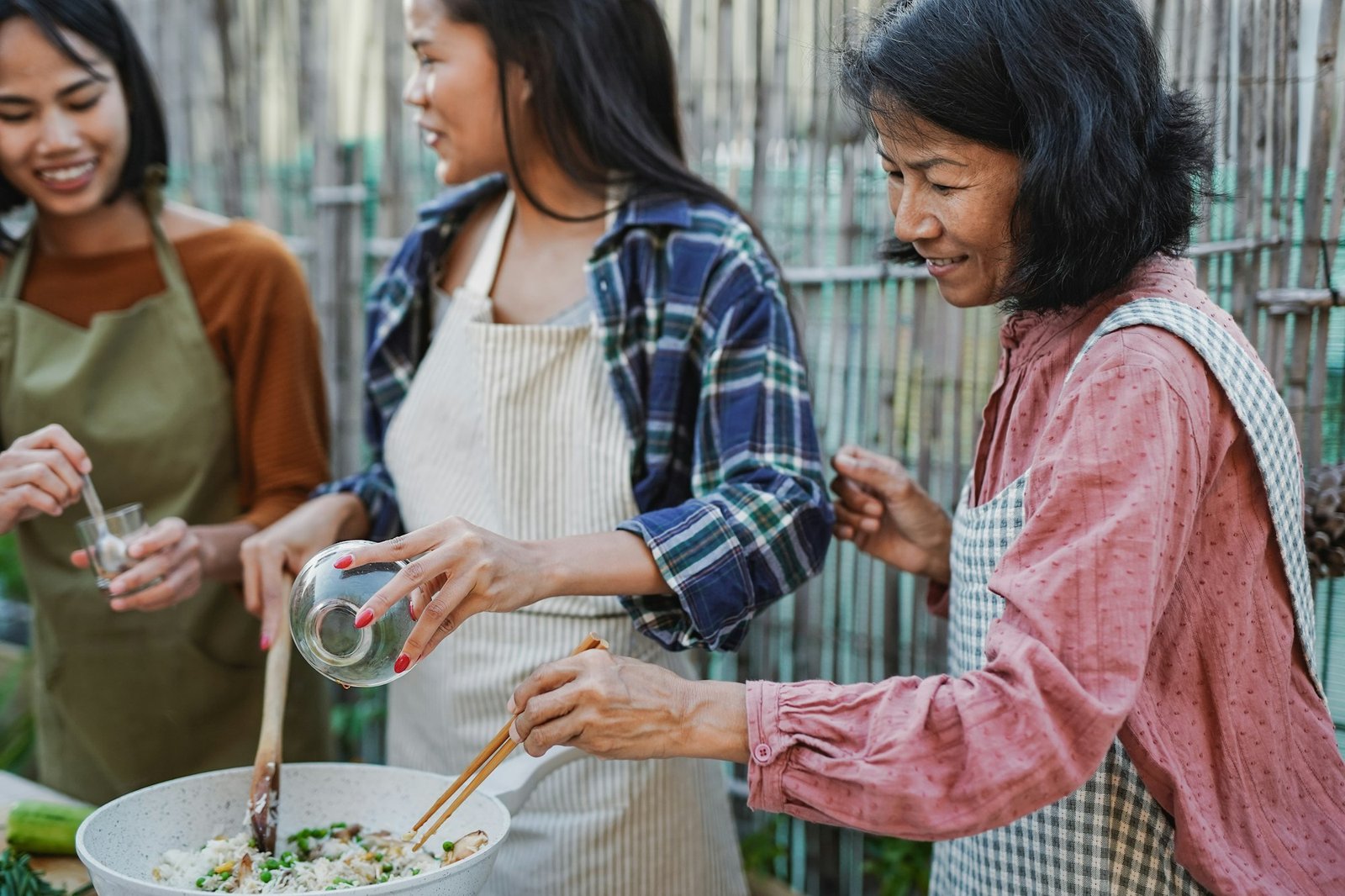 Asian mother and adult daughters cooking together thai rice outdoor - Family and culture concept