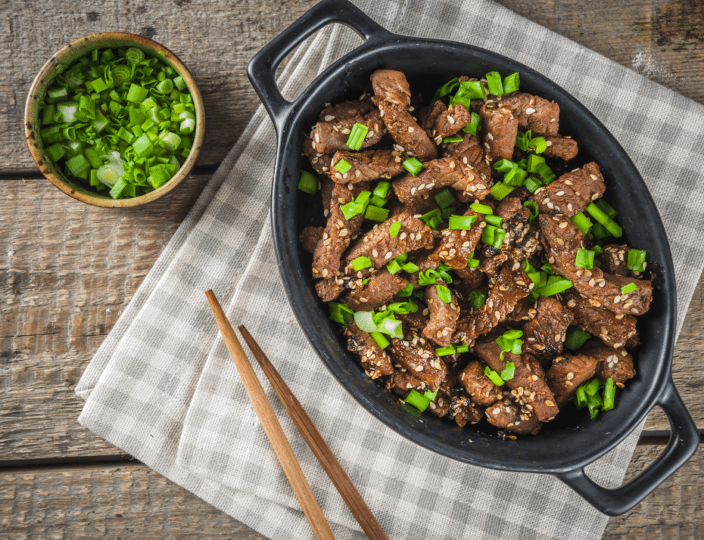 Een bord met heerlijke Bulgogi Beef, een traditioneel Koreaans gerecht bestaande uit dun gesneden rundvlees gemarineerd in een mix van sojasaus, sesamolie, knoflook en gember, gegrild tot perfectie. Geserveerd met verse rijst, sla bladeren en bijgerechten zoals kimchi. Een smaakvolle combinatie van zoet en hartig met authentieke Aziatische smaken.